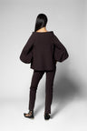 A model shown from the back wearing a dark brown off-the-shoulder top with dramatic balloon sleeves and matching dark brown slim-fit pants, set against a light gray studio background.