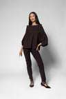 A woman modeling a dark brown off-the-shoulder top with balloon sleeves and matching slim-fit pants, paired with black lace-up flats, against a light gray studio background.