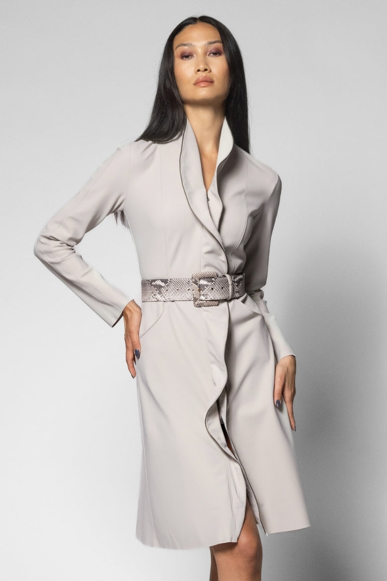 A woman modeling a light gray wrap-style coat with a wide collar, long sleeves, and a textured python belt, photographed against a plain light gray studio background.