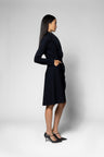 A woman modeling a black long-sleeve knee-length coat, shown from a side profile against a light gray studio background.