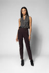 A model stands against a light gray studio background wearing a sleeveless textured gray wrap-style top and dark brown slim-fit trousers with black ankle boots.