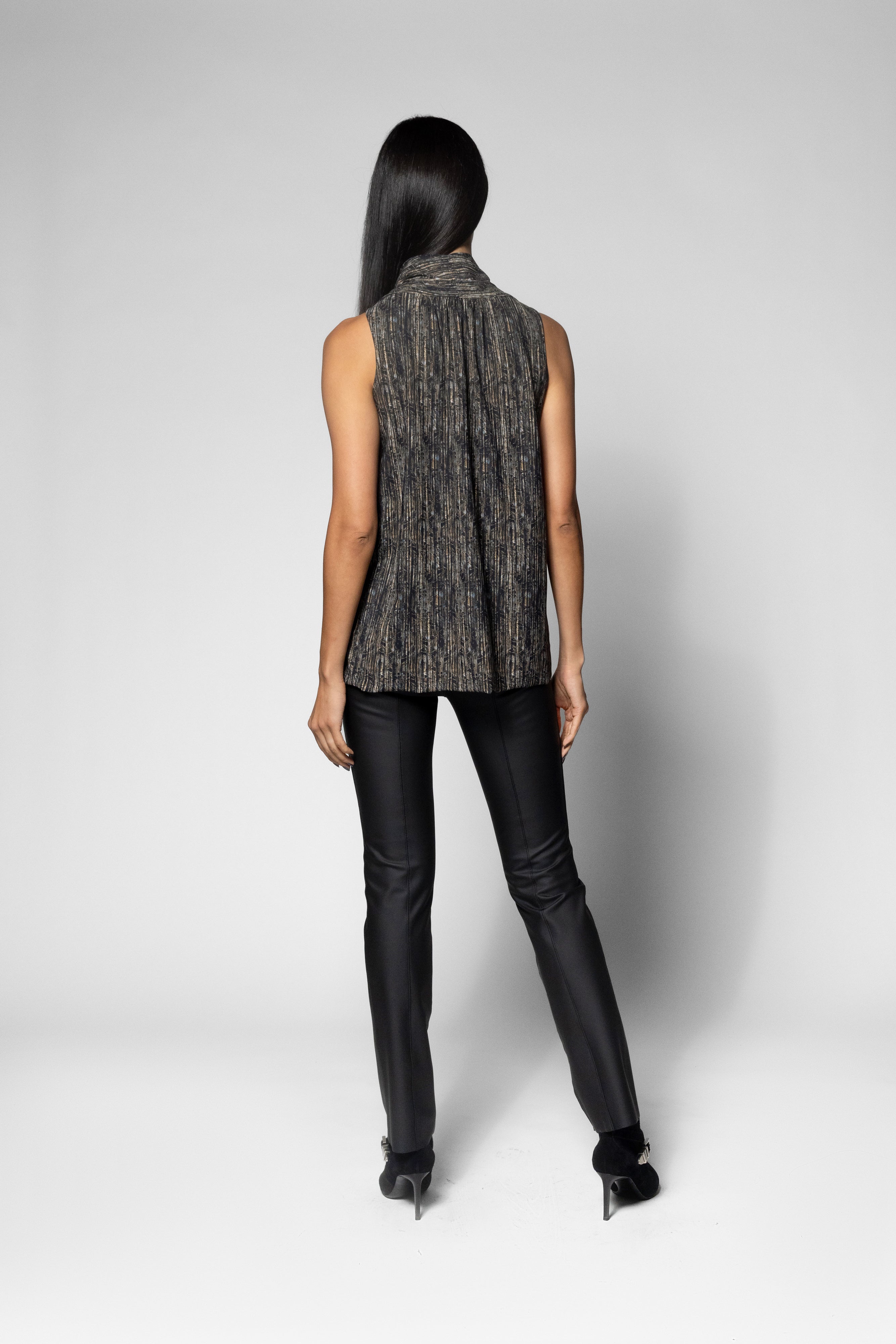 A woman shown from the back wearing a sleeveless textured gray wrap vest, black pants, and black heels against a light gray studio background.