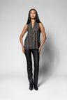 A model stands against a light gray studio background wearing a sleeveless textured top with a dark gray and black mottled pattern, paired with black pants and black ankle boots.