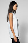 A woman shown in side profile wearing a sleeveless white top and black pants against a light gray studio background.