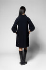 A model viewed from the back wearing a black long-sleeve coat with balloon sleeves and black knee-high boots, set against a plain light gray studio background.