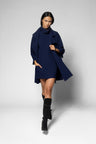 A model walks forward wearing a navy blue coat over a matching navy turtleneck dress, paired with black knee-high boots, against a light gray studio background.