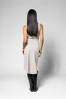 A woman with long, straight black hair is shown from behind, wearing a sleeveless light gray dress and black knee-high boots against a light gray studio background.