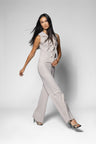 A woman modeling a sleeveless light beige top with ruffle details on the bodice and wide leg pants, paired with black high-heeled sandals, against a light gray studio background.