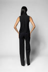 A woman shown from the back wearing a black sleeveless high-neck top and matching black wide-leg trousers against a light gray studio background.