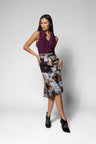 A woman modeling a sleeveless deep purple ruffled top and a high-waisted knee-length skirt and belt with a black, white, and gray abstract floral print, paired with black pointed-toe heels, against a light gray studio background.