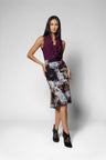 A model wearing a sleeveless ruffled dark purple top and a high-waisted knee-length skirt with a multicolor floral and abstract print, paired with black pointed-toe heels, against a light gray studio background.